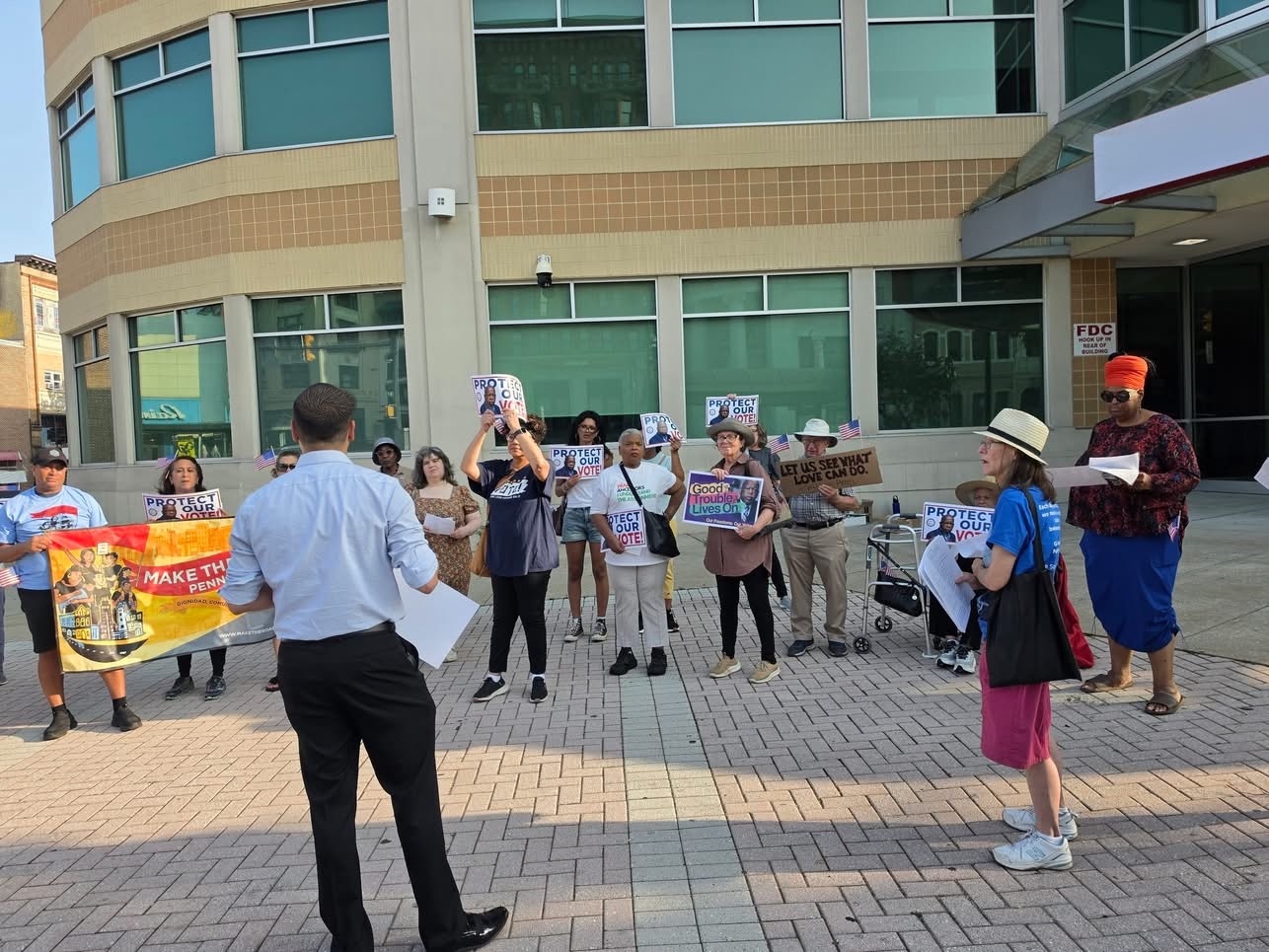 Jaime addressing a group outside holding Protect Our Vote signs